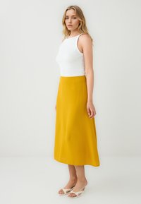 Gonna midi gialla in tessuto leggero con una texture liscia, abbinata a un top bianco fitted e sandali aperti.