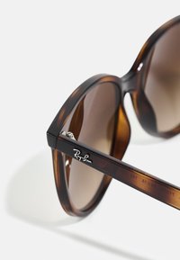Occhiali da sole tartarugati con lenti marroni. Design con montatura ampia caratterizzato da un logo Ray-Ban argento sull'articolazione. Finitura liscia e lucida.