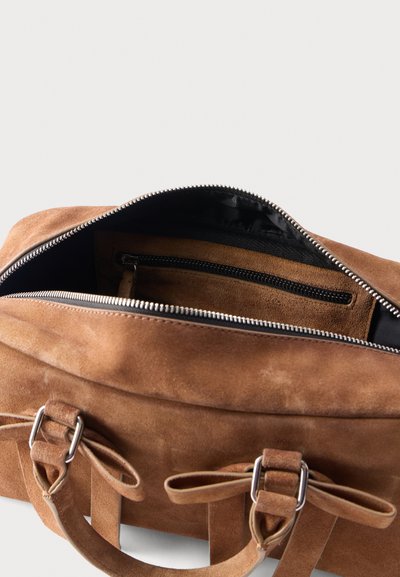 Καφέ σουέντ τσάντα χειρός με ανοιχτό φερμουάρ που αποκαλύπτει εσωτερική τσέπη με φερμουάρ και δύο δεμένους ιμάντες χειρός σε φωτεινό φόντο.