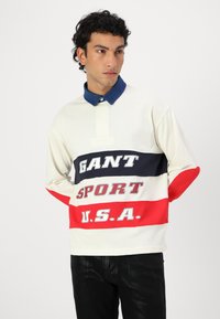 Langermet polo skjorte i off-white med marineblå, rød og grå striper. Har en krage i blå denim og iøynefallende tekstgrafikk på fronten.