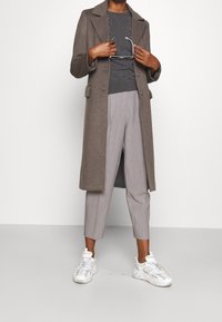 Brązowy wełniany płaszcz, szary sweter oraz jasnoszare spodnie w cienkie prążki, zestawione z białymi trampkami. Płaszcz ma wycięty kołnierz i kieszenie.