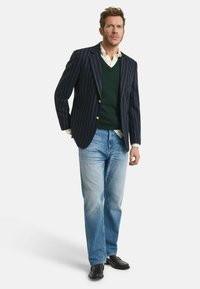 Marine gestreepte blazer met gouden knopen, groene trui, witte blouse, lichtblauwe jeans en zwarte nette schoenen. Slim-casual outfit.