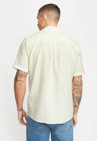 Korte mouw shirt in lichtbeige linnen met een gestructureerde afwerking, voorzien van een achterkant met lende en een boxy ontwerp, gecombineerd met blauwe denim shorts.