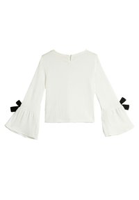 White long-sleeve top with bell sleeves, featuring black bow accents at the cuffs. Textured fabric and a round neckline with a button closure.