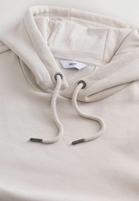Sudadera de color beige claro con capucha ajustable. Fabricada en una tela suave, presenta puntas metálicas en los cordones y una etiqueta interior.