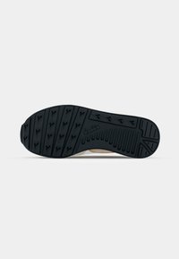 Shoe sole featuring a textured black rubber material with a patterned tread design for traction, complemented by a beige upper edge.
