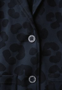 Marineblazer met een zwart luipaardprintpatroon, voorzien van een ronde zwarte knop nabij een zak, gemaakt van een gladde, gestructureerde stof.