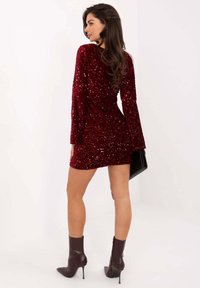 Czerwona mini sukienka z cekinami, z długimi rękawami, dopasowanym krojem i marszczonym tyłem. W zestawieniu z ciemnobrązowymi botkami do kostki i czarną torebką.