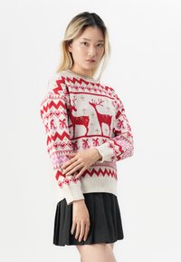 Πλεχτό πουλόβερ με χρώματα κόκκινο και κρέμα, σχέδιο ταράνδου και ζιγκ ζαγκ σχέδια; συνδυασμένο με πλισέ μαύρη φούστα.