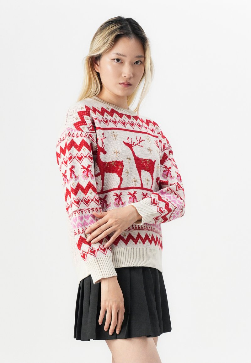 Suéter de punto con una combinación de colores rojo y crema, un patrón de renos y diseños en zigzag; combinado con una falda negra con pliegues.