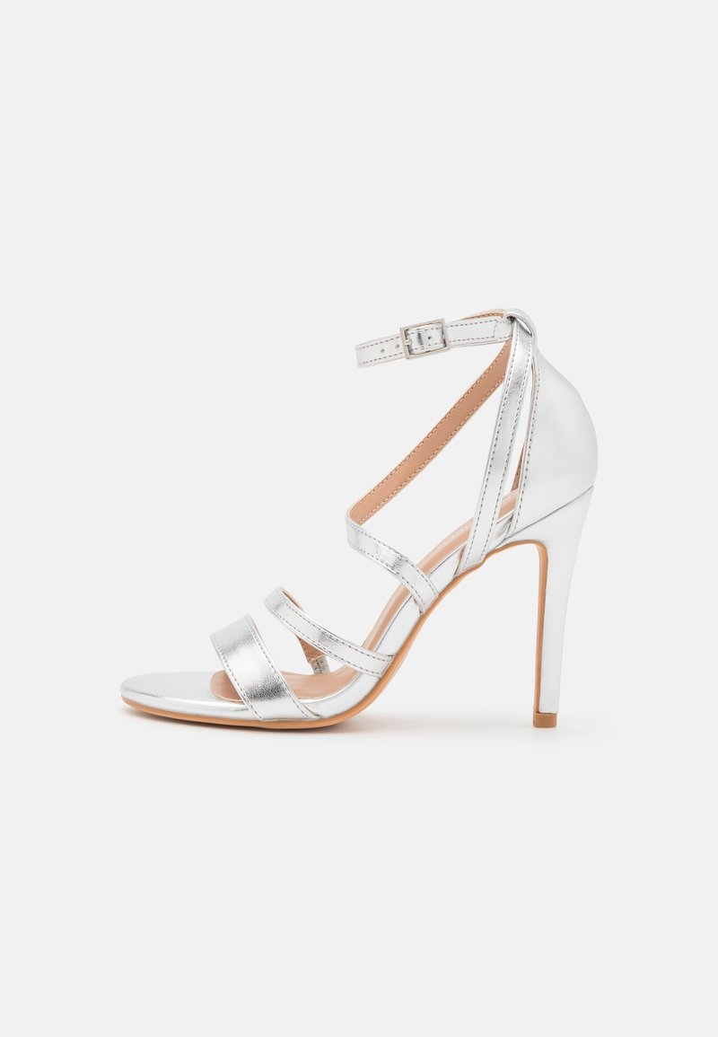 Sandale argentée à talon haut avec bride à la cheville et plusieurs fines brides sur le pied, avec fermeture à boucle et semelle beige.
