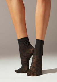 Sorte, gennemsigtige ankelstrømper med et subtilt leopardmønster og en gathered topkant. Den glatte tekstur forstærker det gennemsigtige design.