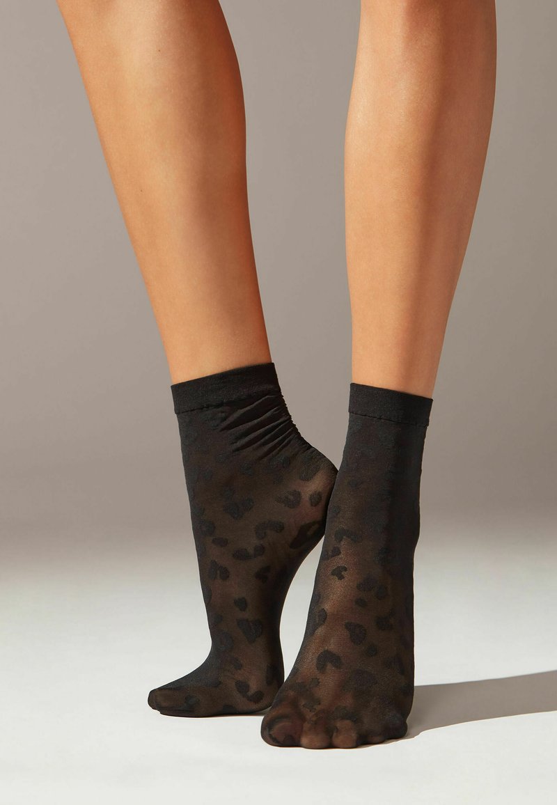 Sorte, gennemsigtige ankelstrømper med et subtilt leopardmønster og en gathered topkant. Den glatte tekstur forstærker det gennemsigtige design.