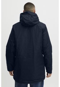 Long navy jacket made of lightweight material, featuring a hood, visible stitching, and a relaxed fit, with long sleeves and a straight cut.
