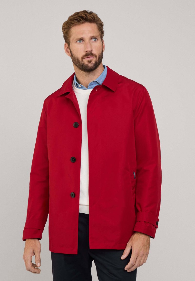 Cappotto rosso impermeabile realizzato in tessuto liscio, con chiusura a bottoni, due tasche laterali e colletto classico.