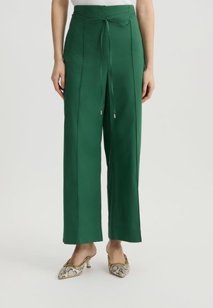 Pantaloni larghi verdi con vita legata, texture liscia e leggero lucido. Accentuati da cuciture laterali, abbinati a tacchi con stampa serpente.