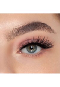 Gros plan sur un œil avec de longs cils sombres et volumineux, un sourcil bien défini et un fard à paupières rose doux sur un teint clair.