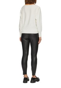Pull en tricot blanc avec taille et poignets côtelés associé à des leggings en cuir noirs. Le mannequin porte des mocassins à plateforme noirs.