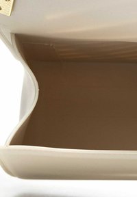 Borsa beige con un'esterno liscio, bordi morbidi e una chiusura dorata; l'interno è di una tonalità più scura di beige con un design spazioso e aperto.