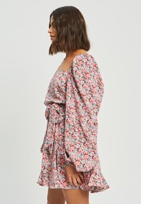 Cvetna obleka z rožnato osnovo, napihnjenimi rokavi in nabrano obrobo. Tkanina ima vzorec manjših modrih in rdečih rož.