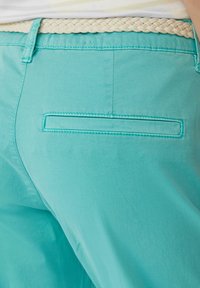 Turquoise broek met een gladde stof, een achterzak met een rechthoekige opening en een gevlochten beige riem om de taille.