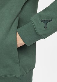 Felpa verde con un tessuto a trama, polsini a coste, tasca a marsupio e logo ricamato in nero sulla manica sinistra.