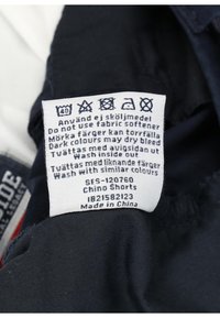 Navy chino shorts with a fabric care label featuring washing instructions in multiple languages and care symbols. Made in China.