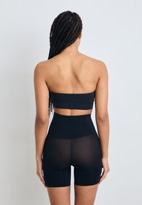 Top negru fără bretele și pantaloni scurți cu talie înaltă, cu o textură netedă și elastică. Pantalonii scurți prezintă o bandă semi-transparentă în spate.