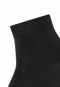 Schwarze Knöchelsocke mit gerippter Textur und elastischem Bündchen. Glatte Stoffoberfläche mit taillierter Form. Keine sichtbaren Muster oder Beschläge.