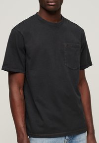 Zwarte korte mouwen t-shirt gemaakt van katoen, met een borstzak en een ronde hals. Heeft een gladde textuur met zichtbare stikseldetails.