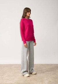 Felroze sweater met lange mouwen, ronde halslijn, gecombineerd met high-waisted lichtgrijze wijde jeans en beige sneakers.