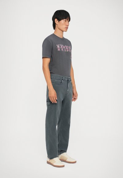 T-shirt grigio con grafica di orso multicolore, abbinato a jeans grigi sbiaditi e sneakers avorio con dettagli marroni. Design semplice e casual.