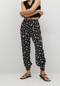 Pantalons noirs à motifs floraux en tissu léger. Dotés d'une taille élastique avec cordon de serrage et de poignets fuselés.