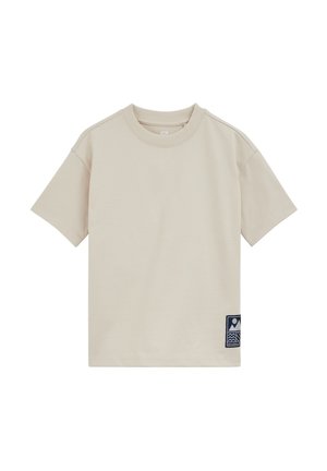 T-shirt beige à manches courtes et col rond avec un petit patch bleu marine présentant des formes abstraites près de l'ourlet inférieur sur le côté gauche.