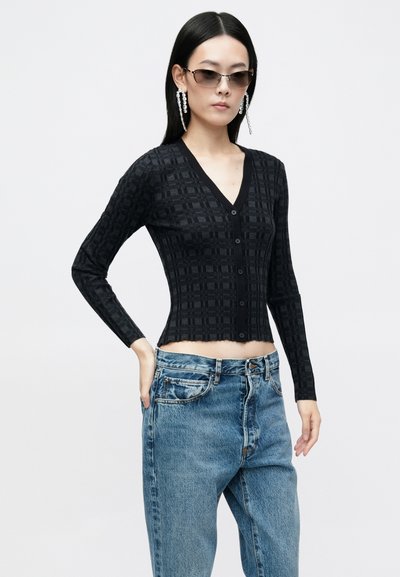 Cardigan noir à motifs en V avec des manches longues et une fermeture à boutons, associé à un jean en denim bleu taille haute avec une coupe décontractée.