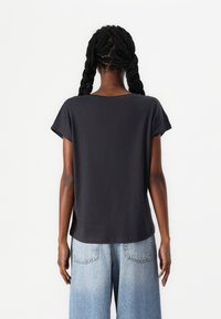 Dark gray short-sleeve t-shirt with a relaxed fit and rounded neckline, tucked into light blue wide-leg jeans, shown from the back.
