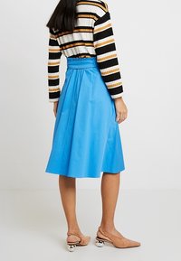 En blå A-linje kjol med en strukturerad midja och slät textur, tillsammans med en svart-och-vit randig tröja, sedd bakifrån.