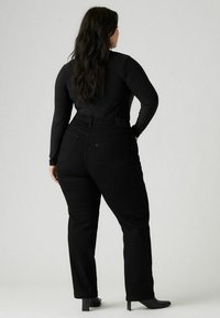 Pantalones de mezclilla negros con corte recto, cinco bolsillos y cintura alta. La tela tiene un acabado ligeramente texturizado.
