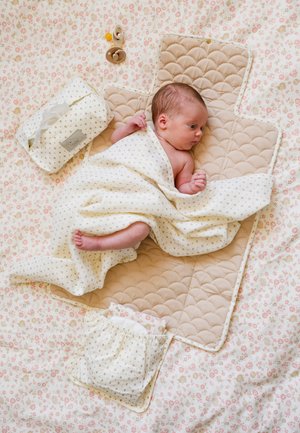 Nyfødt baby pakket ind i et lyst mønstret klæde på en quiltet pusleunderlag med sutter og vådservietter i nærheden på blomsterstof.