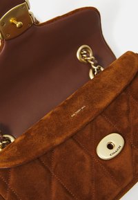 Brown suede quilted handbag with gold chain strap, gold turn-lock closure engraved "Coach," and interior flap labeled "The Tabby Bag."