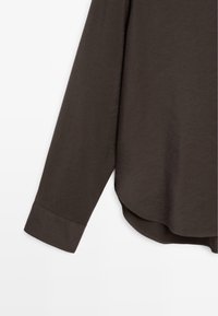 Dunkelbraunes Langarmshirt mit glatter Textur, abgerundetem Saum und maßgeschneiderten Manschetten. Der Stoff wirkt weich und leicht.