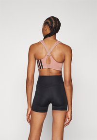 Rosa sports-bh med kryssende stropper og nøkkelhullsdetalj, kombinert med høy midje svarte shorts. Glatt tekstur, minimal merkevare.