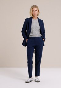 Traje azul marino a medida con un blazer ajustado y pantalones entallados, combinado con un suéter gris claro y zapatillas blancas con acentos negros.