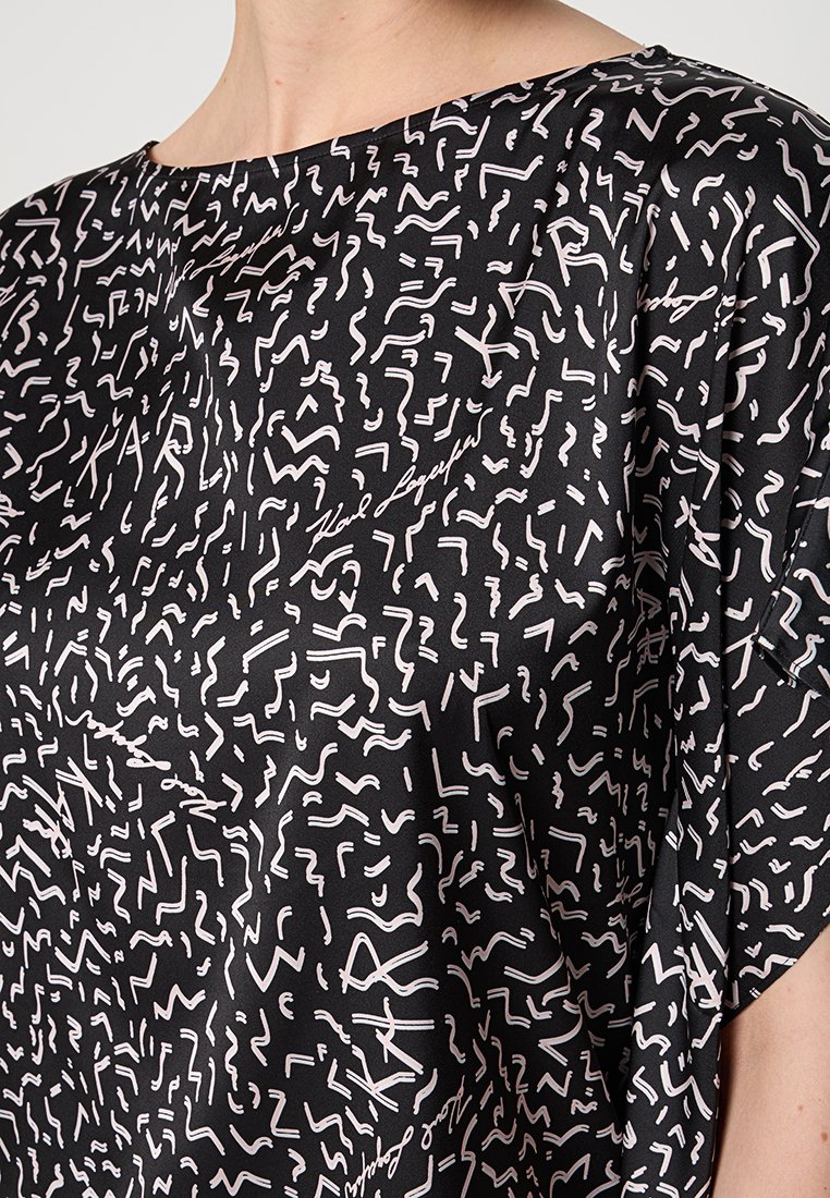 Blouse noire présentant un motif abstrait blanc original et une coupe ample. Tissu doux et lisse avec un décolleté large.