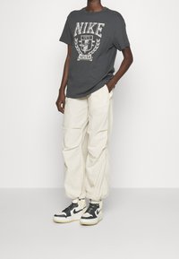 T-shirt gris Nike avec un design graphique, lettrage blanc et manches courtes ; pantalon cargo ample couleur crème ; baskets montantes noir et blanc.