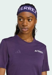 Camiseta deportiva morada de manga corta, con un logotipo blanco de TERREX en el pecho. Textura suave y escote redondo.