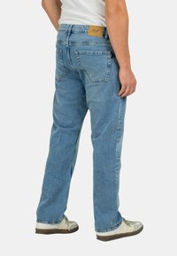 Vaqueros de denim azul claro con corte recto, que cuentan con una parche de cuero beige en la parte trasera de la cinturilla y dos bolsillos traseros.