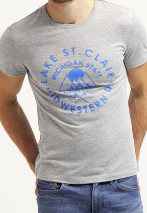 Mężczyzna w jasnoszarej koszulce z niebieskim logo gór oraz tekstem "Lake St. Clair, Michigan State, Midwestern."