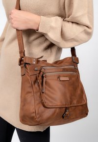 Brun läder crossbody-väska med justerbar rem, framfickor med blixtlås och texturerad yta. Anmärkningsvärda metalldetaljer på fickorna.