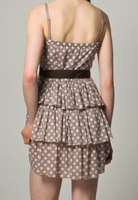 Hnědé šaty s puntíky, s volánkovými vrstvami, tenkými ramínky a širokým tmavým pásem v pase. Lehká tkanina a neformální design.